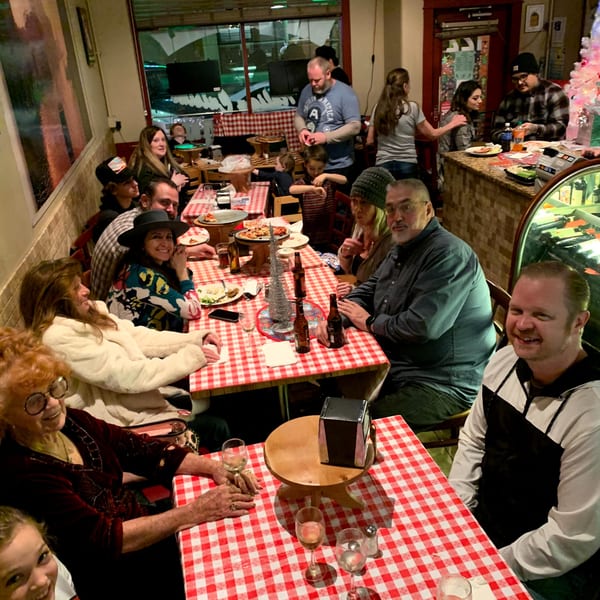 A lively Italian restaurant with families and friends enjoying pizza and drinks at red-and-white checkered tables.