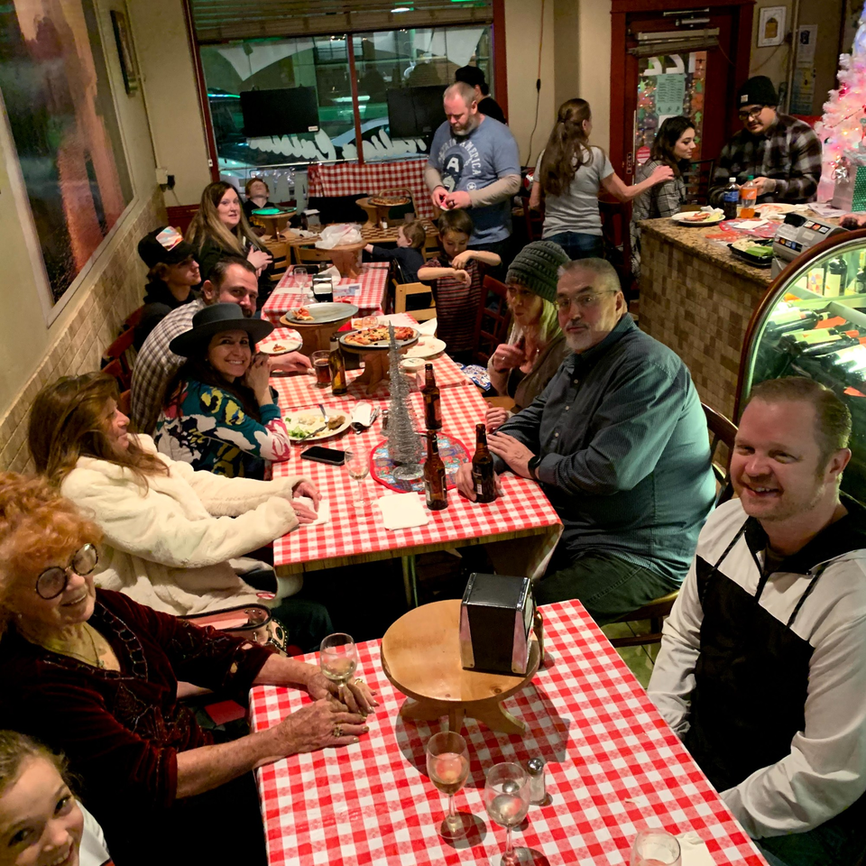 A lively Italian restaurant with families and friends enjoying pizza and drinks at red-and-white checkered tables.