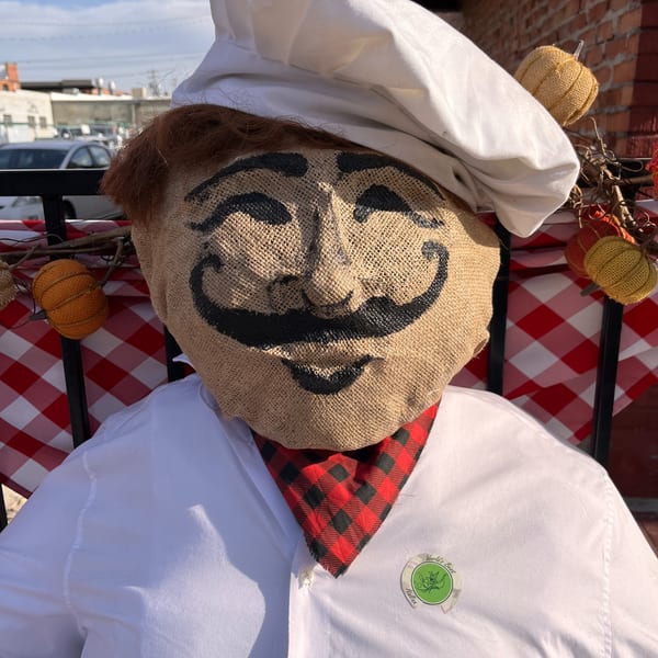 A scarecrow chef with a burlap face, white hat, and red checkered scarf, representing Italian To Go.