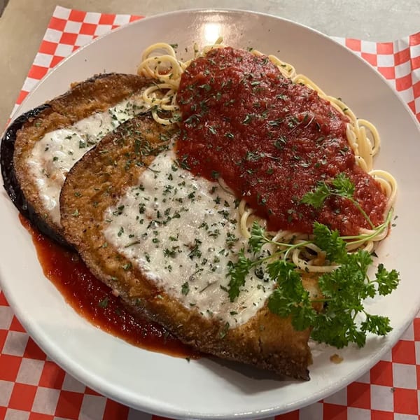 Eggplant Parmesan with spaghetti and marinara sauce, garnished with parsley on a white plate.