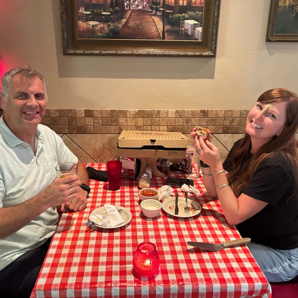 A smiling couple enjoying pizza and drinks at a red and white checkered table at Italian To Go.