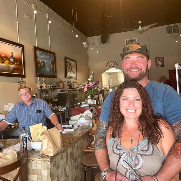 Smiling couple embracing in front of a counter with a man in a blue shirt behind it.