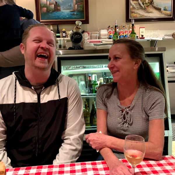 Two happy customers, a man and a woman, laughing at a table with a red and white checkered tablecloth.