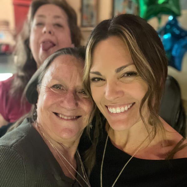Three smiling women, two in the foreground and one playfully sticking out her tongue in the background.