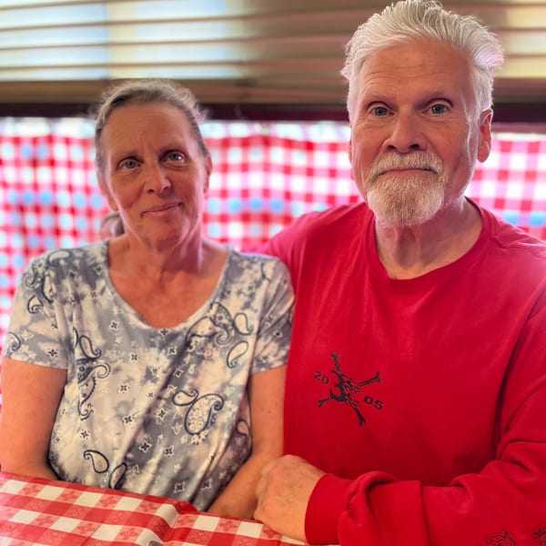 A smiling couple, a woman and a man, sitting at a table with a red and white checkered tablecloth.
