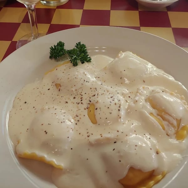 Italian ravioli pasta covered in a creamy white sauce, garnished with parsley and black pepper.