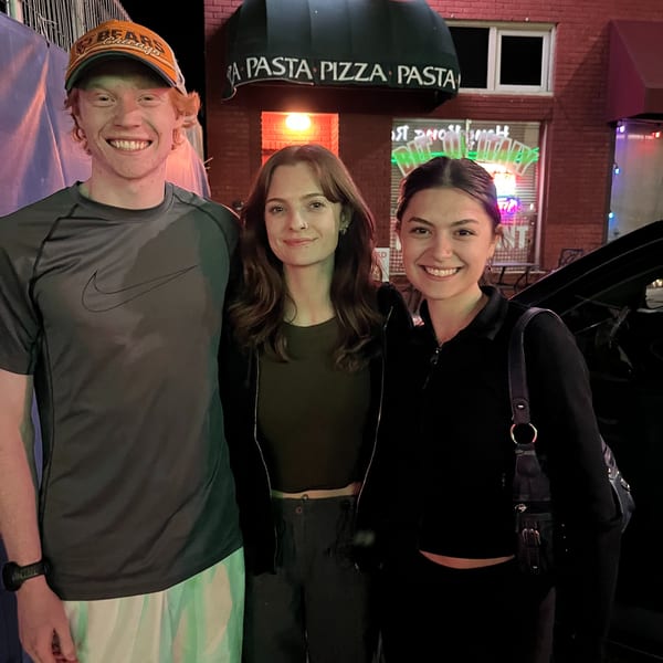 Three smiling young adults stand outside Italian To Go / Bit Of Italy at night.