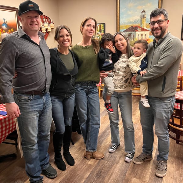 Three couples and two young children smiling for a photo in an Italian restaurant dining room.