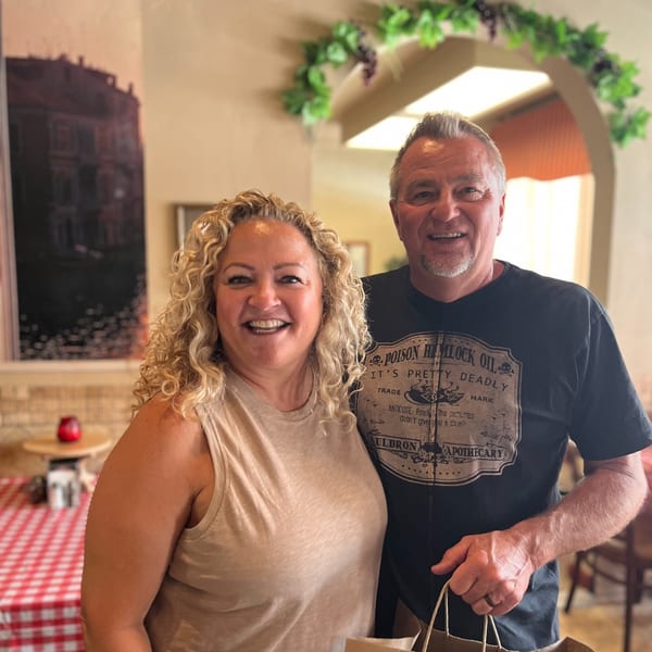 Smiling couple standing in an Italian restaurant, holding a takeout bag.