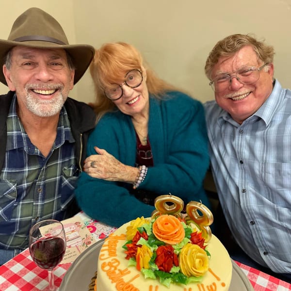 Three smiling people celebrating a birthday with a cake and wine at Italian To Go.