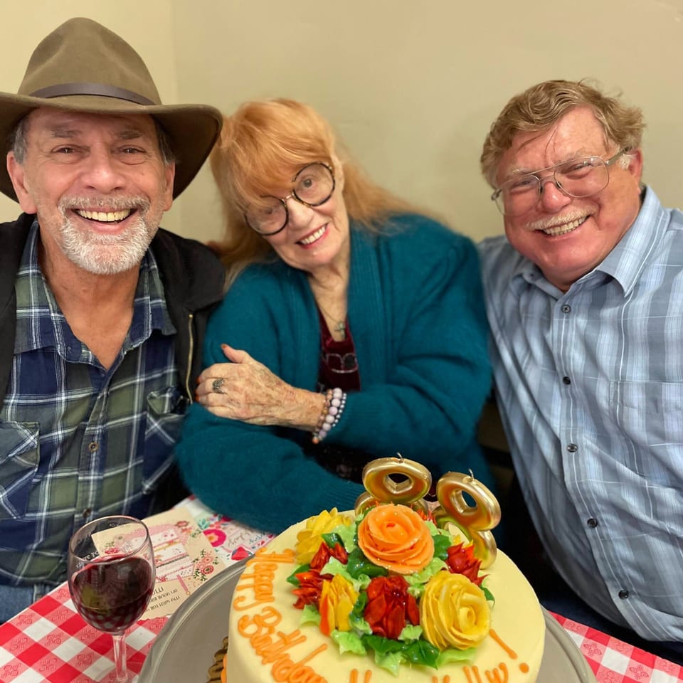 Three smiling people celebrating a birthday with a cake and wine at Italian To Go.