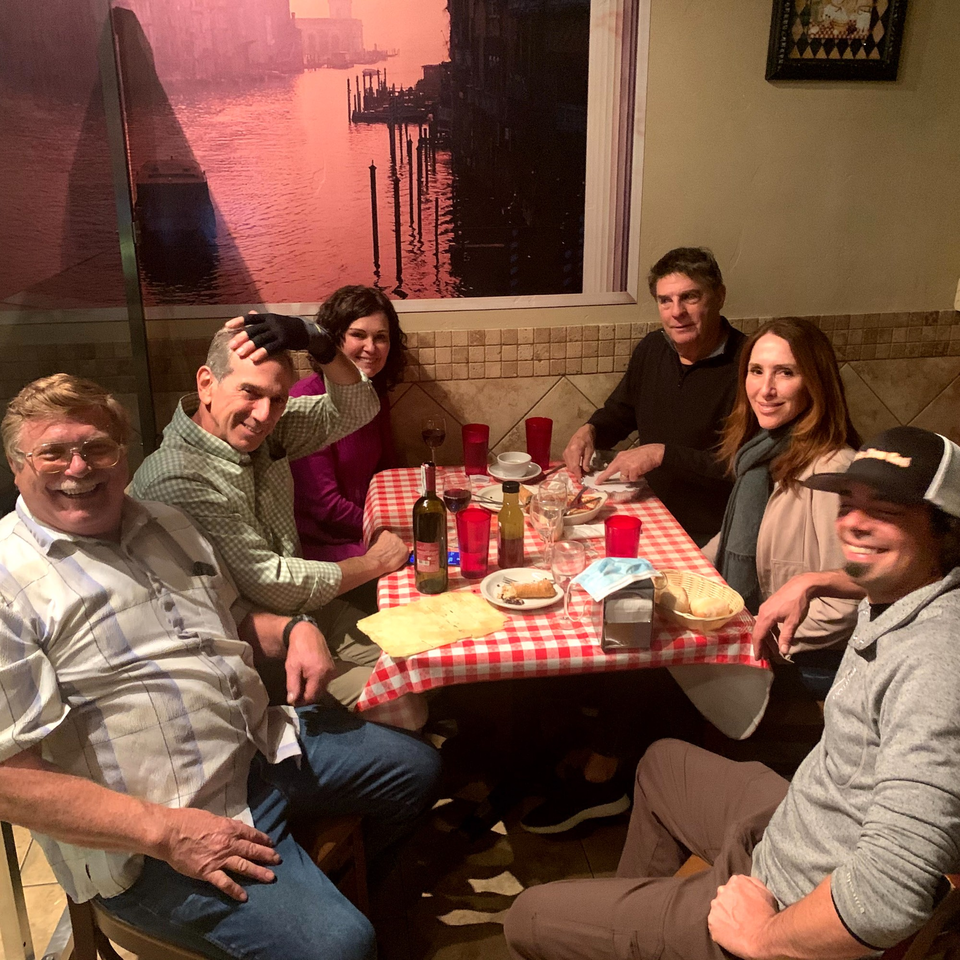 Six happy diners enjoying Italian food and wine at a table with a red checkered tablecloth.
