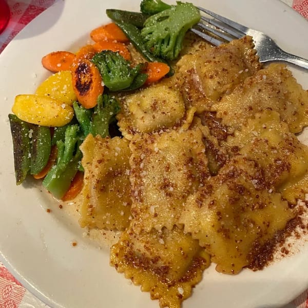 Italian ravioli with parmesan cheese and a side of roasted vegetables on a white plate.