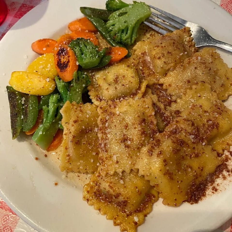 Italian ravioli with parmesan cheese and a side of roasted vegetables on a white plate.