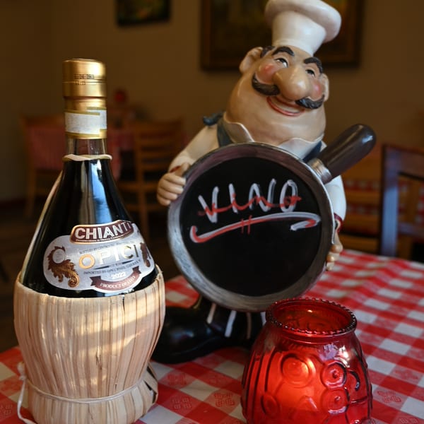Chianti wine bottle, chef figurine holding a "VINO" sign, and red candle on a checkered tablecloth.