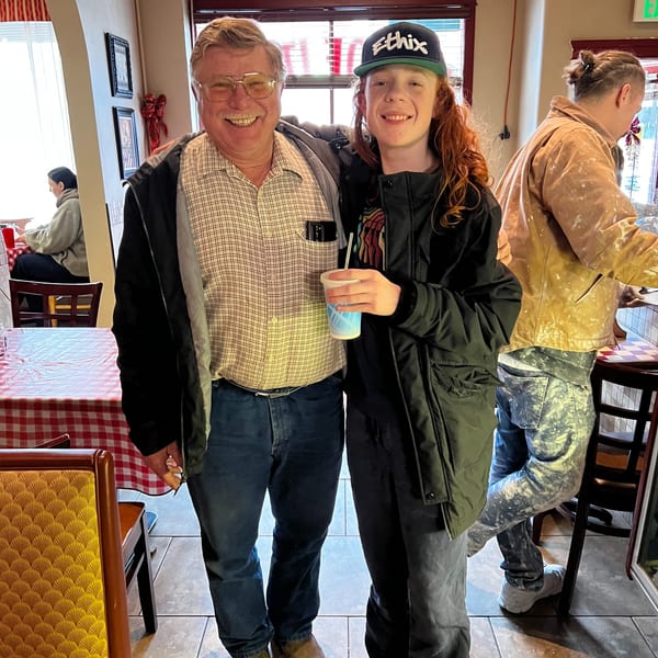 Two men, one older and one younger, smiling at the camera inside the Italian To Go restaurant.