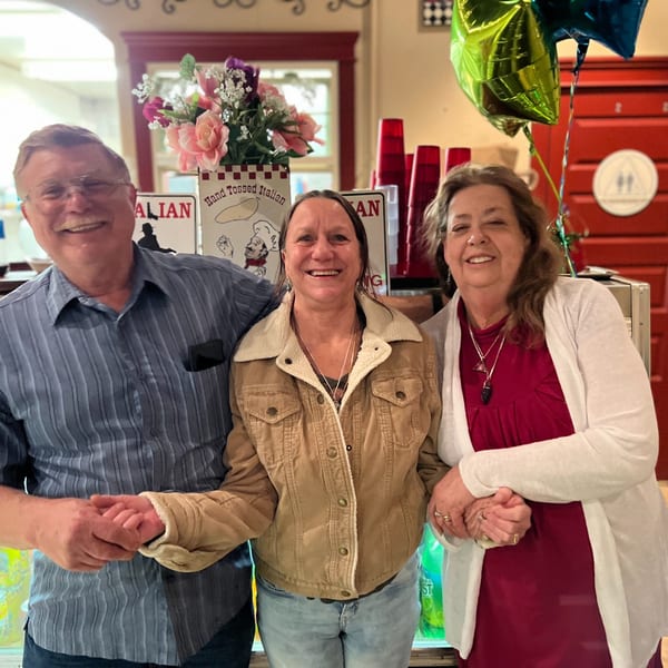 Three smiling people, two women and one man, standing together in an Italian restaurant.