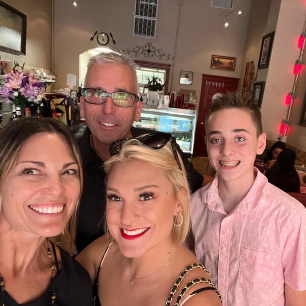 A family of four smiling for a selfie inside the Italian To Go / Bit Of Italy restaurant.