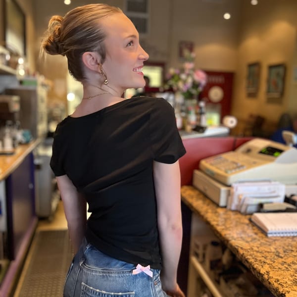 A smiling woman with blonde hair in a bun looks over her shoulder in an Italian restaurant.