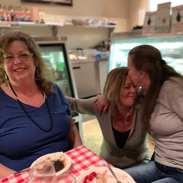 Three women enjoying themselves at Italian To Go / Bit Of Italy, with one kissing another's forehead.