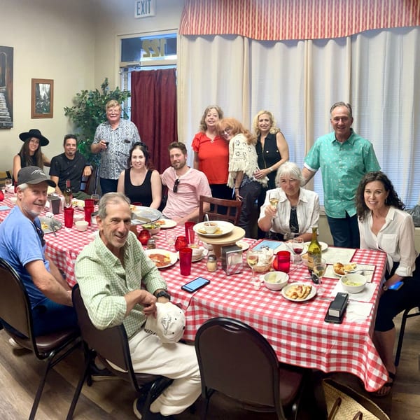 A large group of people gathered around a red and white checkered table, enjoying an Italian meal.