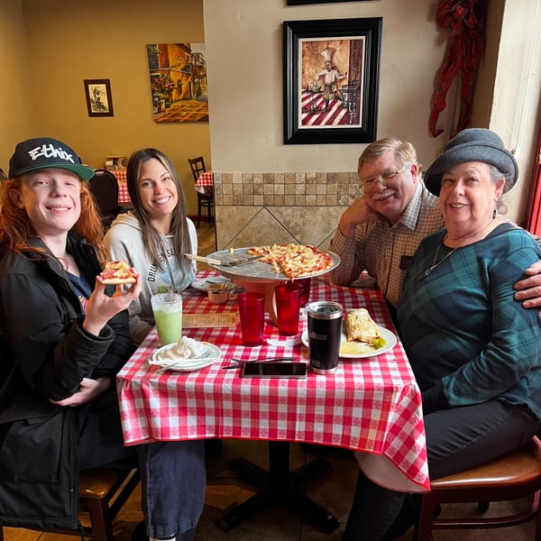 Four happy people enjoying pizza and drinks at a red and white checkered table at Italian To Go.