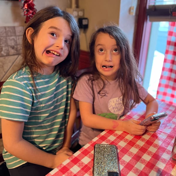 Two young girls making funny faces at a table with a red and white checkered tablecloth.